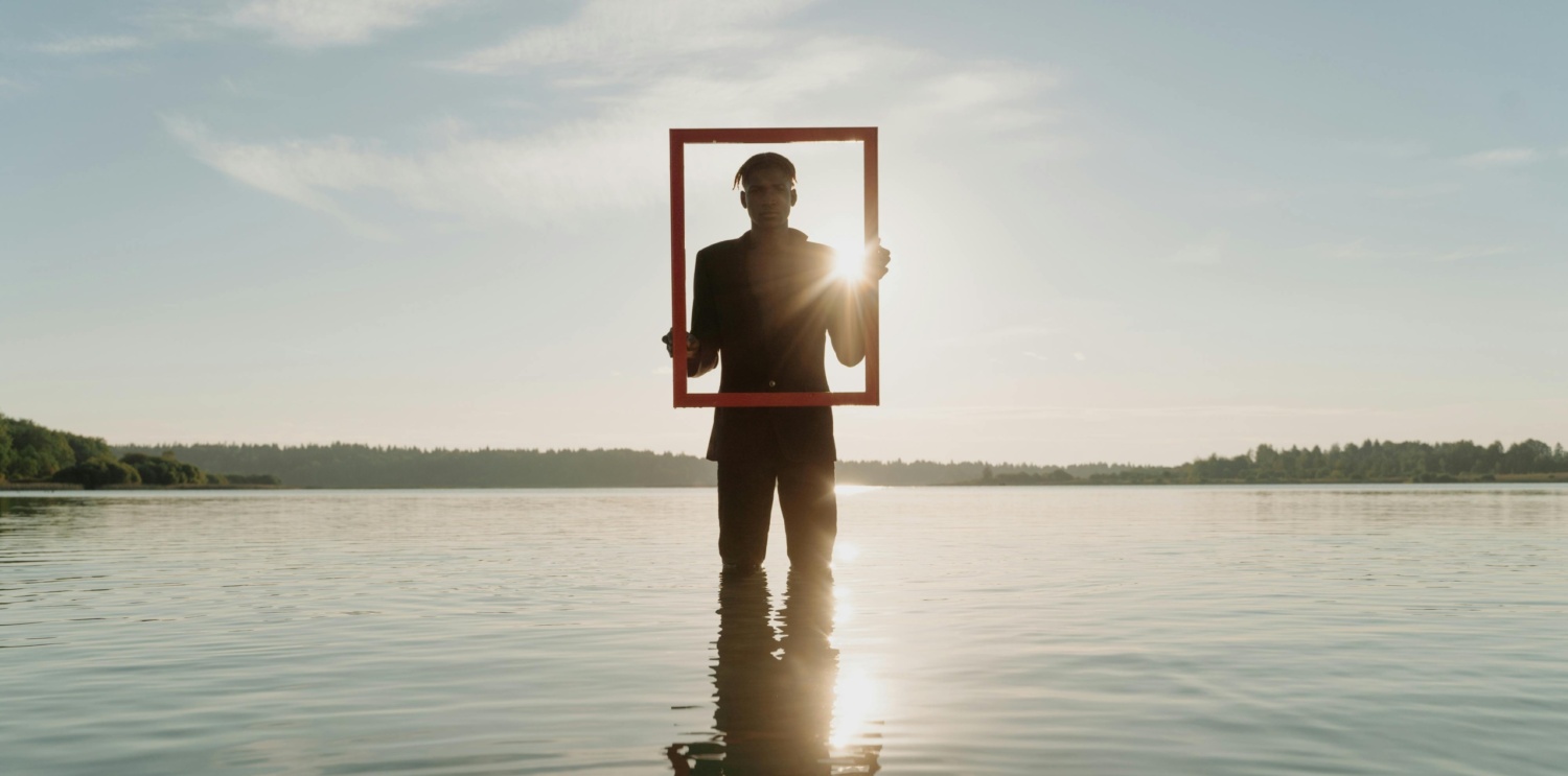 Man standing in a lake holding a frame as the sun sets behind him.
